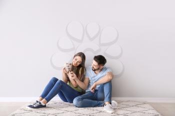 Young couple with cute kitten sitting near light wall�