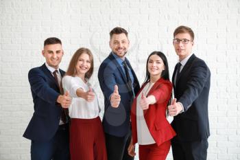 Team of business people showing thumb-up gesture near white brick wall�