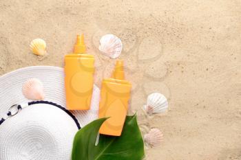 Bottles of sun protection cream, hat and seashells on sand�