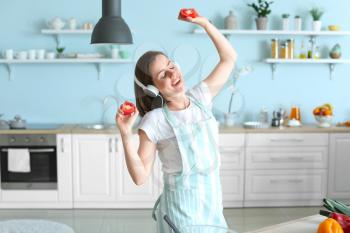 Beautiful young woman listening to music and dancing while cooking in kitchen�