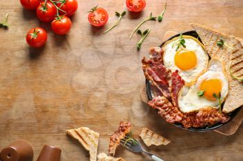 Frying pan with tasty eggs, bacon and toasts on table�