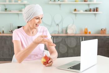 Mature woman after chemotherapy using laptop in kitchen at home�