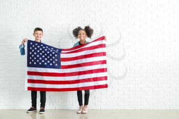 Cute children with national flag of USA near white brick wall�