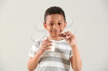 Cute African-American boy with glass of milk and cookie on white background�