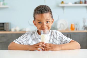 Cute African-American boy with glass of milk at table�