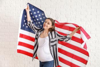 Happy pregnant woman with national flag of USA on white brick background�