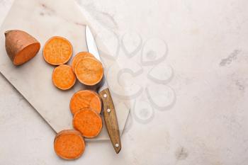 Cutting board and knife with raw sweet potato on light background�