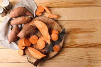 Cutting board and knife with raw sweet potato on wooden background�