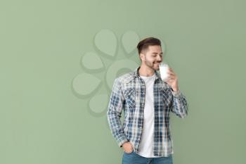 Handsome man drinking tasty milk on color background�