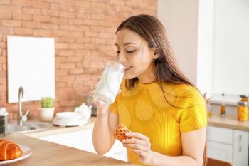 Beautiful woman drinking tasty milk with cookies in kitchen at home�