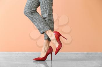 Young woman in high-heeled shoes against color wall�