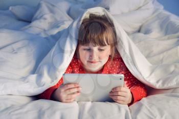 Cute little girl using tablet computer in bed at night�