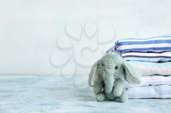 Stack of baby clothes and toy on table against light background�