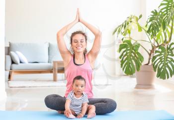 African-American woman with cute little baby practicing yoga at home�