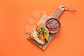 Board with tasty fresh taco and sauce on color background�