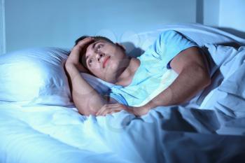 Young man suffering from insomnia while lying in bed at night�