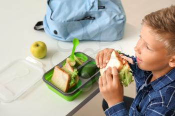 Little schoolboy eating tasty lunch in classroom�