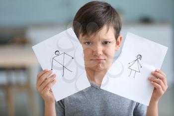 Sad little boy with torn drawing of family at home. Concept of divorce�