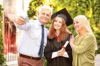 Happy young woman with her parents taking selfie on graduation day�
