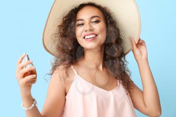 Happy African-American woman with perfume bottle on color background�