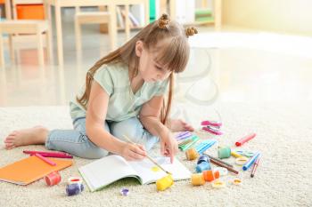 Cute little girl painting while sitting on carpet�