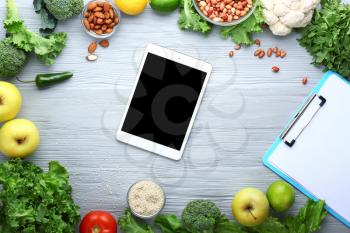 Modern tablet computer with fresh products on wooden background�