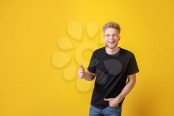 Man in stylish t-shirt showing thumb-up on color background�