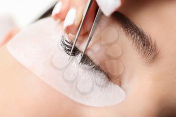 Young woman undergoing eyelash extension procedure in beauty salon, closeup�