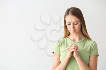 Religious young woman praying on white background�