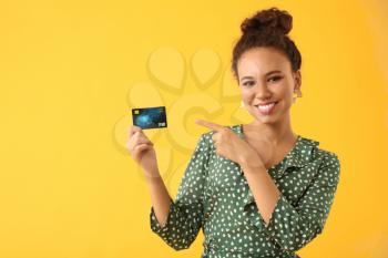 Happy African-American woman with credit card on color background�