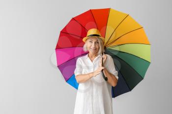 Stylish mature woman with umbrella on light background�