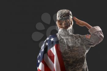 Saluting female soldier with USA flag on dark background, back view�