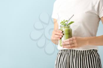 Young woman with tasty smoothie in mason jar on color background, closeup�