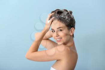Beautiful young woman washing hair against color background�