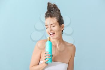 Beautiful young woman using bottle of shampoo as microphone against color background�