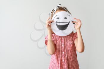 Little girl hiding face behind drawn emoticon on light background�
