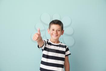 Portrait of happy little boy showing thumb-up gesture on color background�