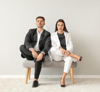 Stylish young couple sitting on bench near white wall�
