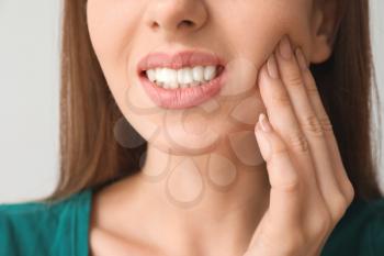 Young woman suffering from toothache against light background, closeup�