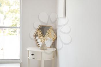 Mirror and vase with golden tropical leaves on table near white wall�