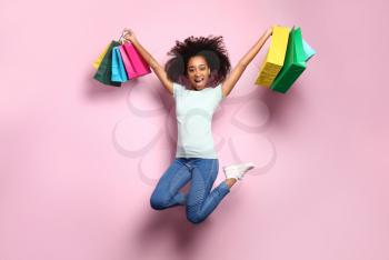 Portrait of jumping African-American woman with shopping bags on color background�