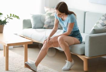 Young woman suffering from pain in knee at home�