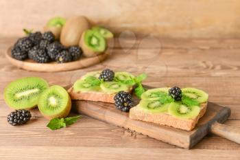 Tasty sandwiches with kiwi and blackberry on wooden table�