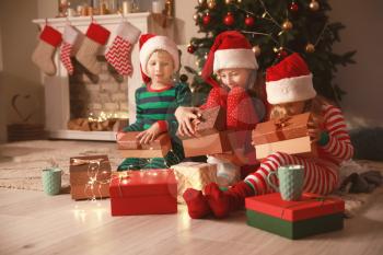 Cute little children opening Christmas gifts at home�