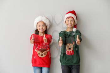 Funny children in Christmas sweaters showing thumb-up on light background�