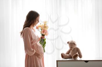 Beautiful pregnant woman with flowers near window�