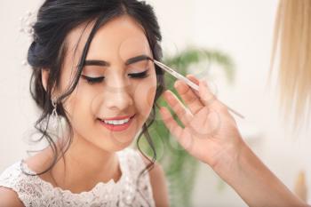Professional makeup artist working with young Asian bride at home�