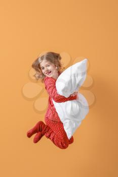 Jumping little girl in pajamas and with pillow on color background�