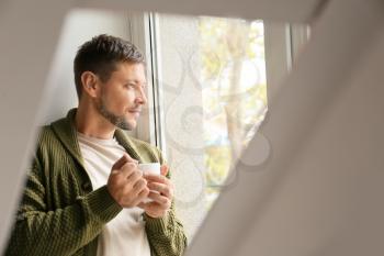 Man with cup of tea relaxing near window at home�