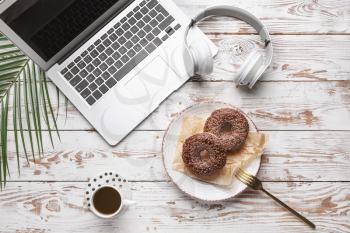 Tasty donuts with laptop, headphones and cup of coffee on white wooden table�